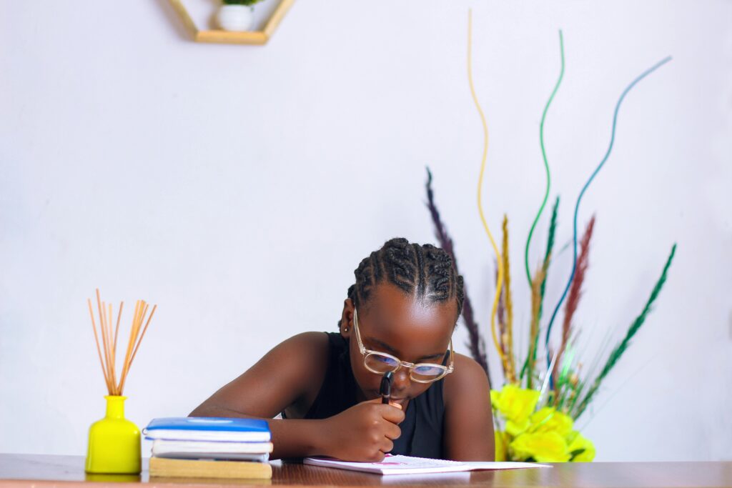 A young African American girl concentrating on her studies at a desk indoors, surrounded by colorful decor.