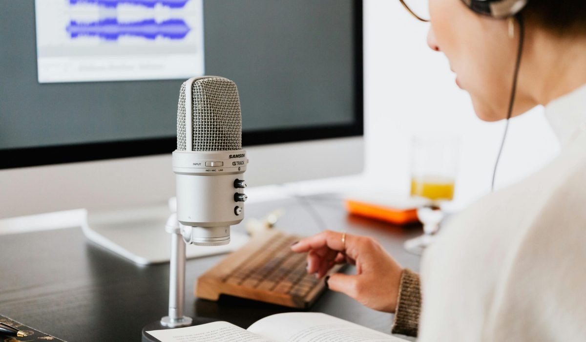 Person wearing headphones reading from a book with a microphone. Ideal for podcasts.