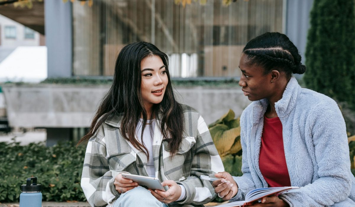 Two young women studying together outdoors, sharing ideas and friendship.